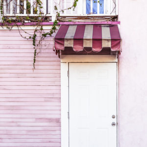A white door surrounded by pink wooden panels, pink stucco, and a pink striped awning