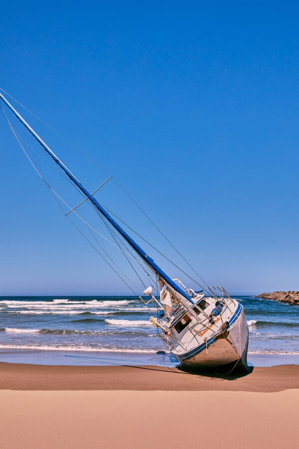 A beached sailing ship on its side in the sand.