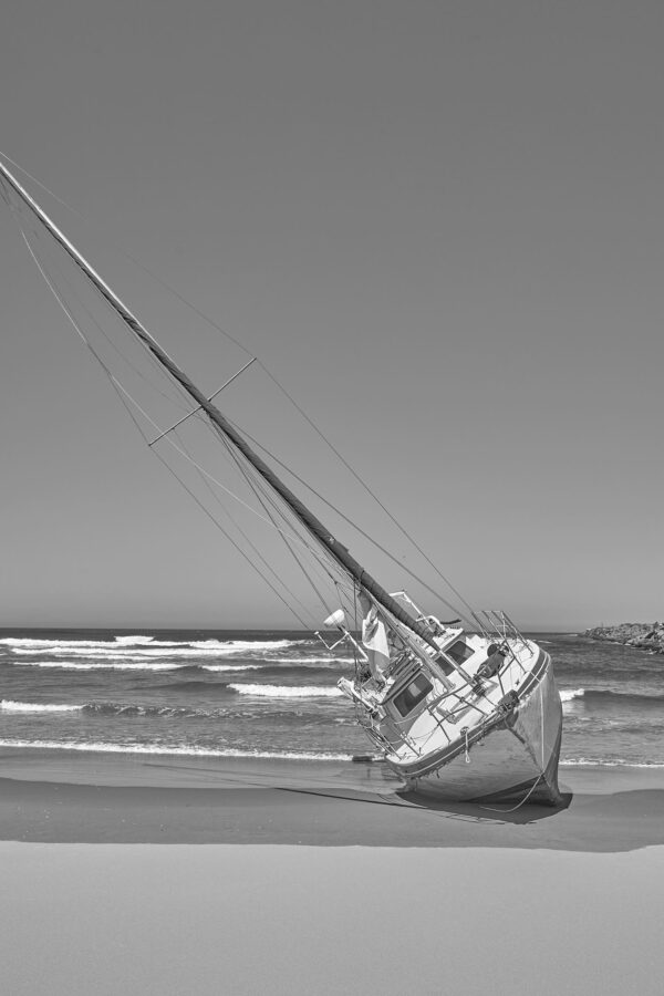 A black and white photo of a beached ship on it's side in the sand.